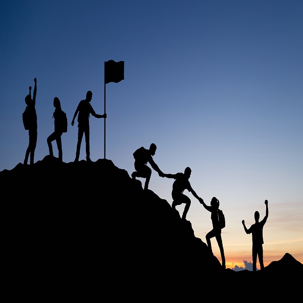 Silhouette of people helping each other hike up a mountain at su